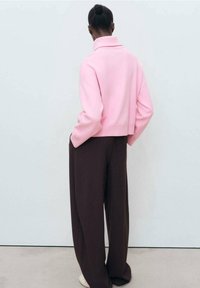 Pull rose court à col montant, associé à un pantalon large marron. Texture lisse, design minimaliste, coupe décontractée.