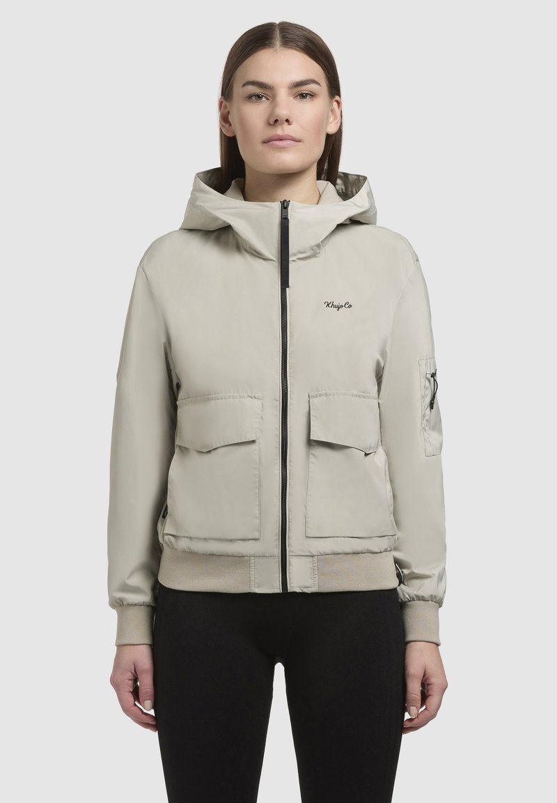 Light grey hooded jacket made of smooth fabric. Features a front zipper, two large front pockets, and ribbed cuffs. Minimalist design with logo detail.