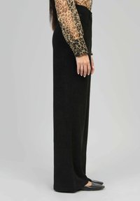 Pantalons larges noirs en tissu doux, avec une texture lisse et une taille haute. Assortis à un haut à imprimé léopard.