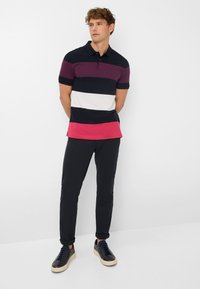 Herrliches Polohemd mit vertikalen Streifen in Marineblau, Burgunderrot, Weiß und Rosa; kombiniert mit schwarzen, slim-fit Hosen und dunklen Sneakers.