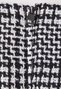 Svart och vit tweedtyg med en strukturerad, vävd mönster och lösa trådar. Dragkedja i glänsande silvermetall i mitten.