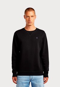 Felpa nera realizzata in morbido misto cotone con polsini e orlo a costine. Presenta un logo discreto sul petto e un classico scollo rotondo.