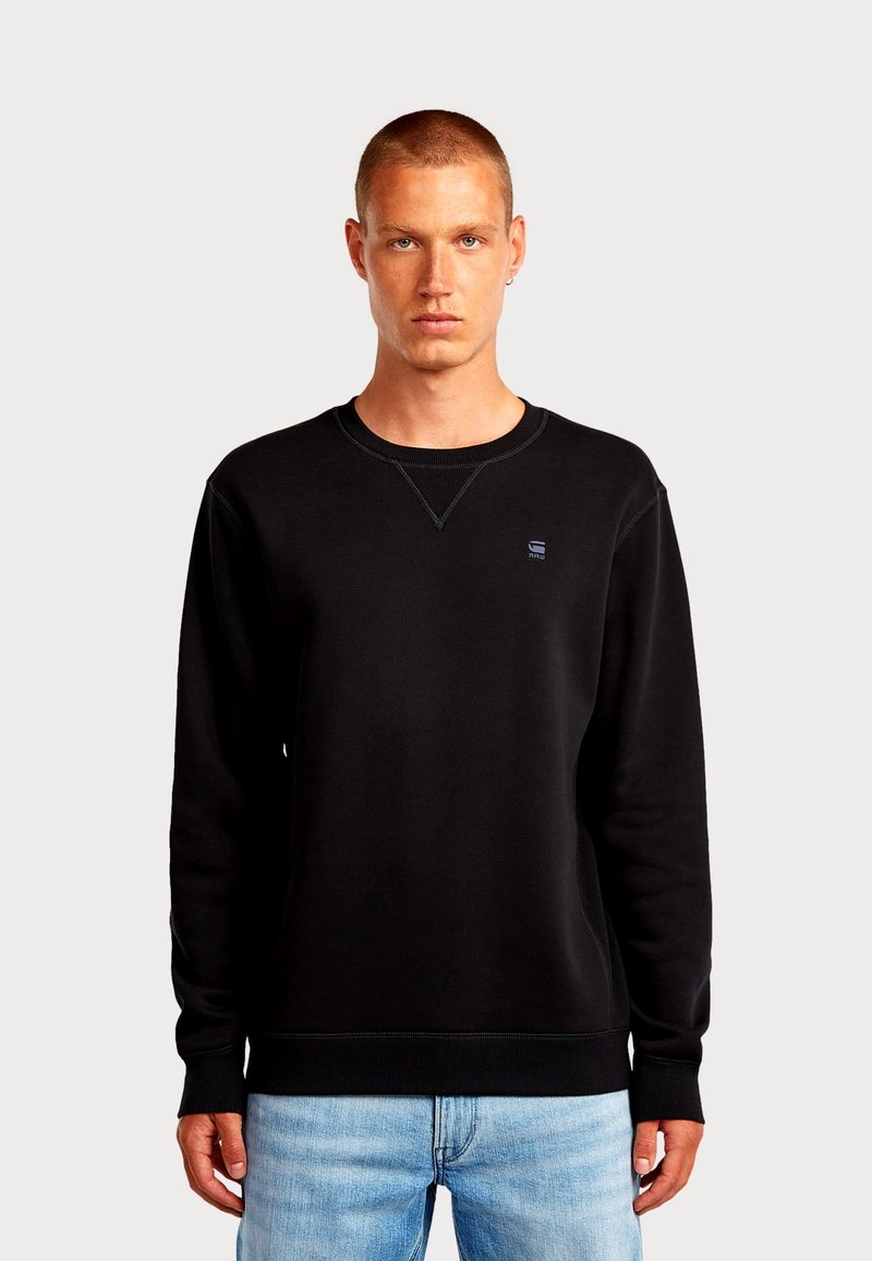 Felpa nera realizzata in morbido misto cotone con polsini e orlo a costine. Presenta un logo discreto sul petto e un classico scollo rotondo.