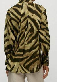 Long-sleeve shirt in a glossy fabric featuring a green and brown tiger stripe pattern, with a back yoke and button cuffs.