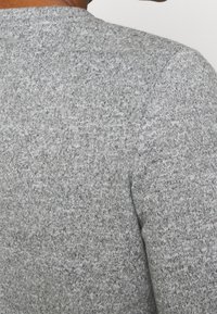 Grau gestrickter Pullover mit weicher Textur, enganliegendem Design und klassischem Rundhalsausschnitt, durchzogen von einem melierten Muster.