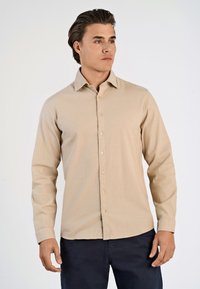 Camicia beige a maniche lunghe realizzata in un tessuto morbido con bottoni sul davanti e colletto, caratterizzata da bottoni marrone chiaro e una vestibilità su misura.
