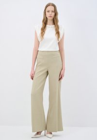 Witte mouwloze top met een parelaccent bij de halslijn, gecombineerd met lichtbeige wijd broek. De look wordt aangevuld met witte hakken.