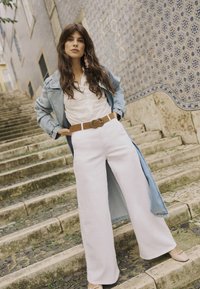 Denim plašč preko belih širokih hlač, v kombinaciji z lahko bluzo in rjavim pasom. Roza uhani s posebnim poudarkom dopolnjujejo obleko.