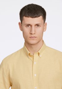 Lichtgele button-up shirt gemaakt van een gestructureerde stof. Beschikt over een klassieke kraag en witte knopen, met een eenvoudig en strak ontwerp.