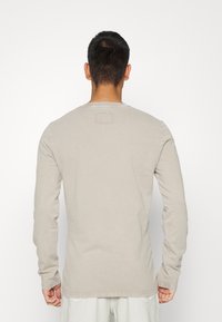 Camisa de manga larga color beige claro con cuello redondo y detalle cosido en la parte posterior. Textura suave y diseño minimalista.