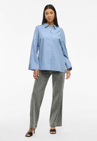 Hellblaues Button-up-Hemd mit langen Ärmeln, kombiniert mit grauen gestreiften weit geschnittenen Hosen und schwarzen Absatzsandalen.