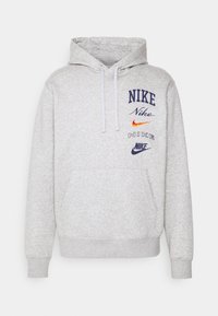 Grå hoodie av mjukt tyg som har en framstående känguruficka, justerbar dragsko och flera broderade Nike-logotyper i olika färger.
