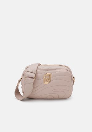 Small beige crossbody bag with wavy stitching, gold decorative logo, adjustable wide strap, and zipper closure on top.
