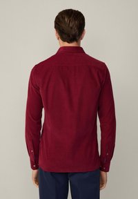 Camicia a maniche lunghe color bordeaux realizzata in tessuto testurizzato. Presenta un colletto appuntito, polsini con bottone e un orlo dritto con dettagli di cucitura.