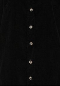 Tissu en velours côtelé noir avec une rangée verticale de cinq boutons ronds de couleur claire, chacun cousu avec quatre trous en forme de « X ».