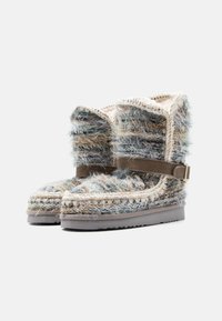 Pūkainas potīšu zābaki ar zilu, bēšu un pelēku krāsu apvienojumu; ietver zamšādas siksniņu un fakturētu vilnas augšdaļu. Gumijas zole labākam saķerei.