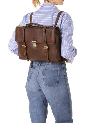 Zaino in pelle marrone con chiusura a pattina, accessori in metallo e spallacci regolabili. Superficie texture e forma rettangolare classica.
