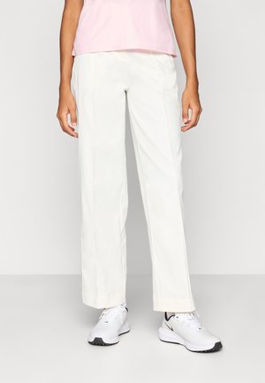 Bela široke hlače z gladko teksturo in čistimi linijami, kombinirane z belimi športnimi čevlji. Zgornji del je svetlo roza barve.