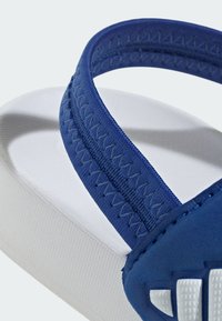 Chancla azul con una correa texturizada con costuras y una base para el pie blanca. Detalles notables incluyen lados acolchados y acentos con el logo.
