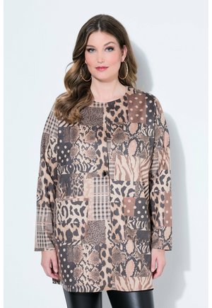 Vrouw met golvend haar draagt een patchworkjack met dierenprints, stippen en ruitpatronen, gecombineerd met zwarte leren broek.