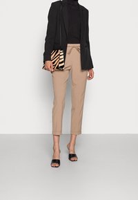 Blazer nero su un dolcevita nero, pantaloni beige a sigaretta e una borsa a strisce zebrate. Sandali neri completano l'outfit.