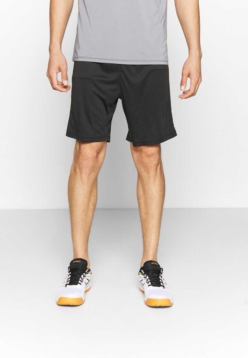 Sorteidrettsshorts laget av lett materiale, med elastisk linning og sidelommer, sammen med hvite og svarte joggesko.