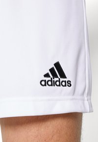 Witte sportshorts van gladde stof, met een zwart geborduurd Adidas-logo aan de linkerkant onderaan.