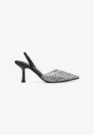 Zapato negro de tacón bajo tipo kitten heel con tira trasera y puntera puntiaguda adornado con strass plateados y negros y tachuelas.