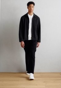 Veste noire à bouton, polo blanc, pantalon noir et baskets blanches. Texture lisse, coupe moderne, design minimaliste.