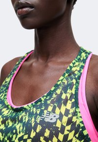 Κοντινό πλάνο ενός ατόμου που φοράει αθλητικό τοπ με σχέδιο νέον πράσινο και μαύρο, με ροζ περιθώριο και λευκό λογότυπο New Balance.