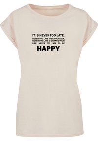 Light pink short-sleeved t-shirt featuring bold black text with motivational phrases, including "IT'S NEVER TOO LATE" and "HAPPY."