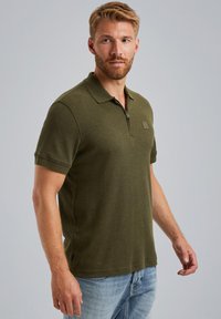 Polo majica u maslinasto zelenoj boji od mješavine pamuka, s kragnom, zatvaranjem na zip i suptilnom oznakom na prsima. Kratki rukavi i regularni kroj.