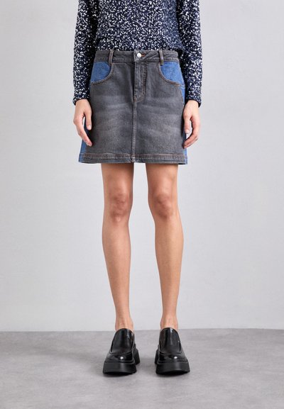 Denim nederdel med en falmet grå krop og blå sidepaneler, der har en mellemhøj talje, forlommer og synlig syning. Sorte slip-on sko på.