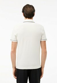 Vitt polo-shirt med svart kant på krage och ärmar, slät textur, korta ärmar och rak skärning, sedd bakifrån.