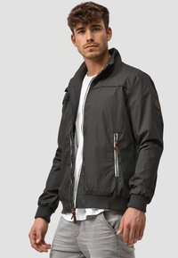 Black bomber jacket with a zip front, ribbed cuffs, and a stand collar. Features brown leather accents and a zippered pocket.
