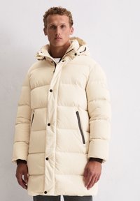 Pufferjack in off-white met een capuchon, voorzien van een horizontaal doorgestikt ontwerp, drukknoopsluiting aan de voorkant en twee zijritszakken.
