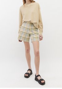 Sudadera beige de corte relajado, combinada con pantalones cortos de cuadros de cintura alta en tonos amarillos y verdes. Sandalias de plataforma negras completan el look.