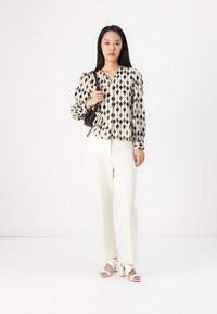 Long-sleeve blouse with a cream and navy diamond pattern, paired with white textured wide-leg trousers and open-toe block-heeled sandals.