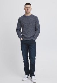 Maglione navy lavorato a maglia con motivo testurizzato, abbinato a jeans denim scuri e sneakers bianche con strisce nere. Outfit casual.