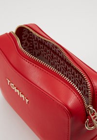 Czerwona saszetka na zamek błyskawiczny ze złotym zamkiem i logo TOMMY, wnętrze w wzór z powtarzającymi się białymi i czerwonymi literami "TH".