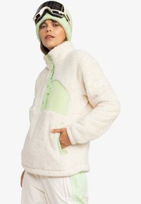 Fleece pullover in off-white with mint green accents, featuring a half-zip front, side pockets, and a soft textured finish.