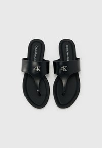 Sorte slidesandaler laget av glatt lær med thong-design, med en metallisk Calvin Klein-logo og flate såler.