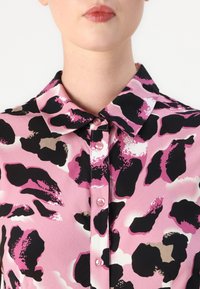Ροζ μπλούζα με γιακά, διακοσμημένη με μεγάλο μαύρο και ροζ λεοπάρ πατρόν. Έχει μικρά ροζ κουμπιά και λεία υφή υφάσματος.