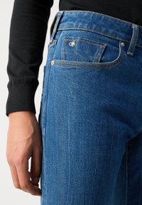 Mørkeblå denim jeans har en lige pasform med markante syninger, en møntlomme og et lille logo på frontlommen.