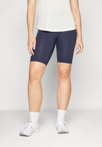 Mörkblå cykelshorts i elastiskt material, med en slät textur och midjehöjd, parat med vita träningsskor och strumpor.