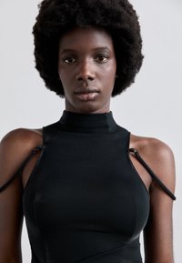 Vestido negro sin mangas con escote alto, tirantes ajustables y un acabado texturizado. El diseño ajustado resalta la silueta.