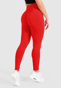 Leggings alti rossi realizzati in un tessuto elasticizzato, caratterizzati da una texture liscia e un design aderente, abbinati a sneakers bianche.