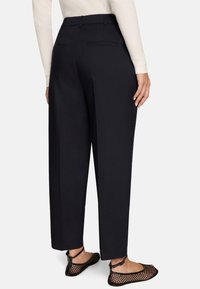 Pantalon noir à jambes larges avec une coupe ajustée, doté de deux poches arrière et d'une texture lisse, associé à des ballerines en résille noire.