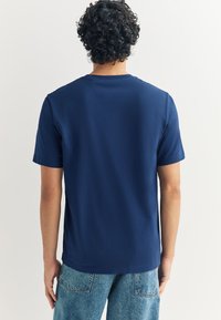 Námornícky modré tričko s krátkym rukávom, bavlnený materiál, dizajn s okrúhlym výstrihom, hladká textúra, v kombinácii s vyblednutými džínsami.