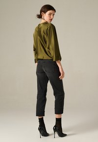 Top satin vert olive à manches trois-quarts, associé à un jean noir court et des chaussures à talons en vernis, vu de dos.